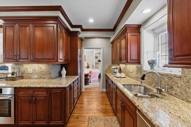 kitchen featuring sink, stainless steel appliances, ornamental molding, light stone countertops, and light wood-type flooring