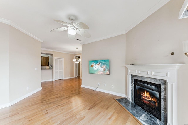 unfurnished living room featuring light hardwood / wood-style floors, crown molding, a premium fireplace, and ceiling fan with notable chandelier