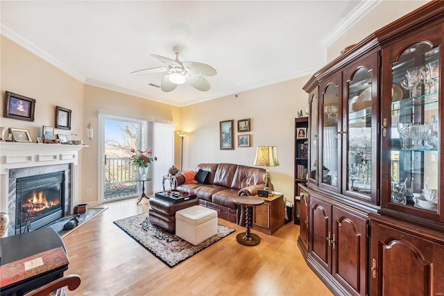 living room featuring a premium fireplace, ornamental molding, light hardwood / wood-style flooring, and ceiling fan