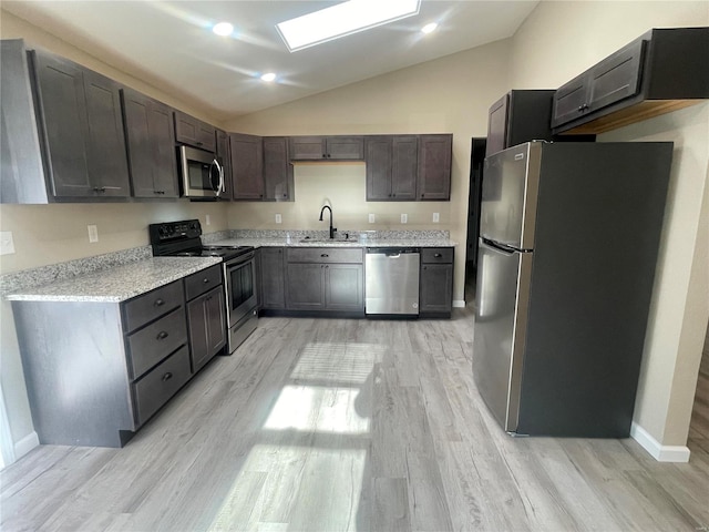 kitchen featuring sink, vaulted ceiling with skylight, appliances with stainless steel finishes, dark brown cabinets, and light hardwood / wood-style floors