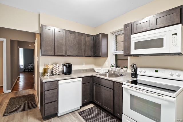 kitchen with dark brown cabinets, sink, white appliances, and light wood-type flooring