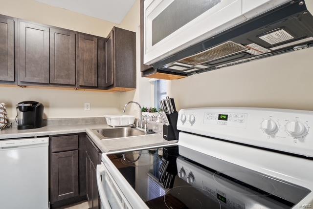 kitchen with dark brown cabinets, white appliances, and sink