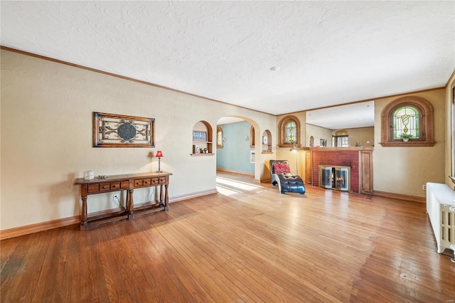 miscellaneous room with a brick fireplace, radiator heating unit, a textured ceiling, and light hardwood / wood-style flooring