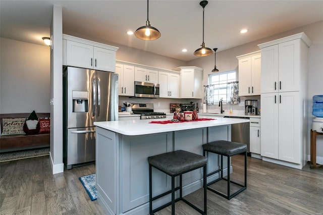 kitchen with appliances with stainless steel finishes, white cabinetry, hanging light fixtures, a center island, and dark hardwood / wood-style flooring