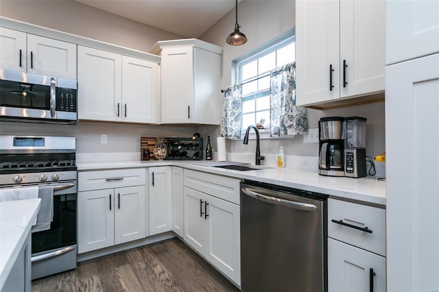 kitchen featuring dark wood-type flooring, sink, decorative light fixtures, appliances with stainless steel finishes, and white cabinets