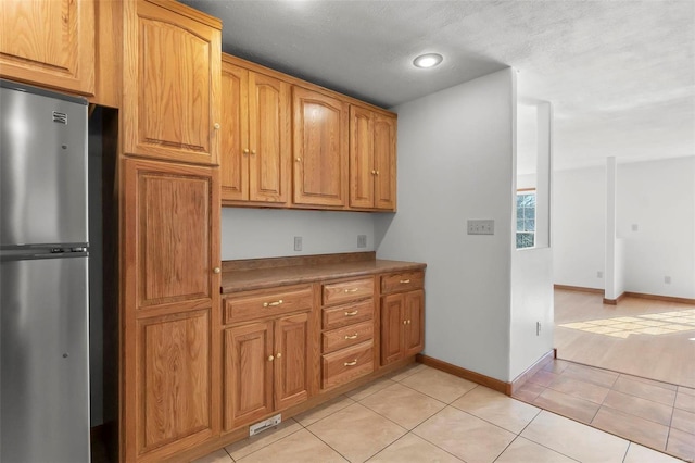 kitchen with stainless steel fridge, light tile patterned flooring, and a textured ceiling