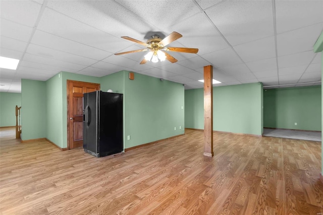 basement featuring ceiling fan, a drop ceiling, light hardwood / wood-style floors, and black refrigerator with ice dispenser