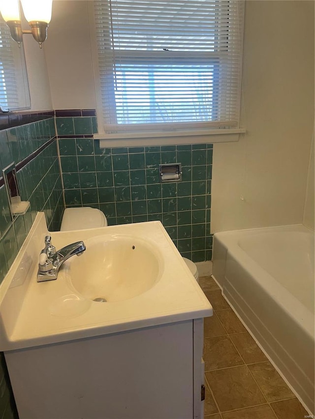 bathroom featuring tile patterned flooring, vanity, a bath, and tile walls