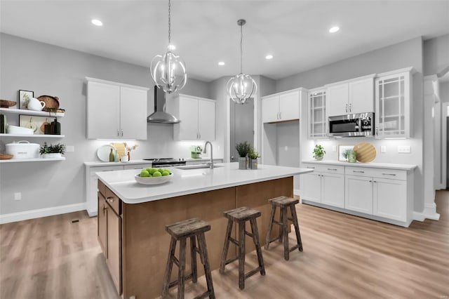 kitchen with appliances with stainless steel finishes, white cabinetry, wall chimney exhaust hood, and an island with sink