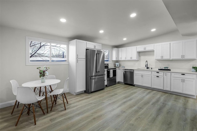 kitchen featuring vaulted ceiling, stainless steel appliances, white cabinetry, and light hardwood / wood-style flooring