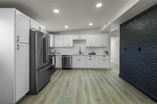 kitchen with appliances with stainless steel finishes, white cabinetry, lofted ceiling, and sink