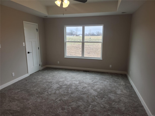 carpeted spare room with a raised ceiling and ceiling fan