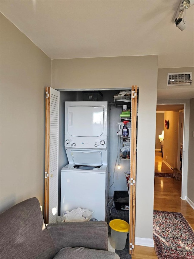 clothes washing area with hardwood / wood-style flooring and stacked washer and clothes dryer