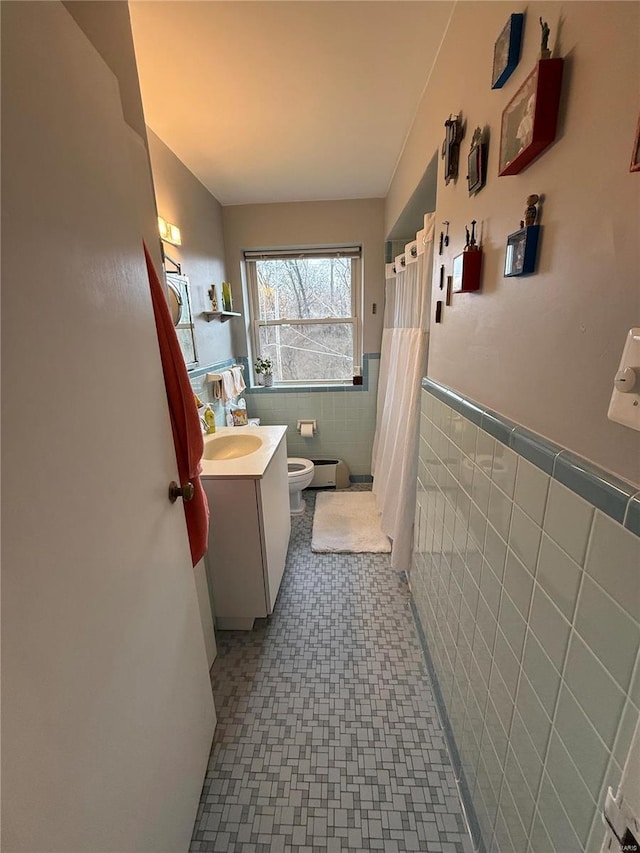 bathroom with walk in shower, vanity, toilet, and tile walls