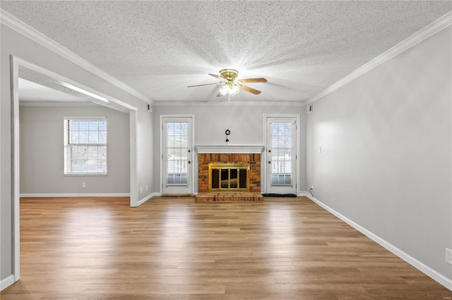 unfurnished living room with light wood-type flooring, a textured ceiling, ceiling fan, crown molding, and a fireplace