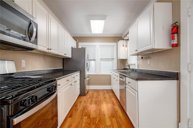 kitchen featuring white cabinetry, sink, light wood-type flooring, appliances with stainless steel finishes, and ornamental molding