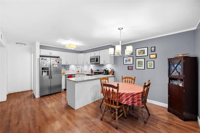 kitchen with stainless steel appliances, pendant lighting, an inviting chandelier, light hardwood / wood-style flooring, and white cabinets