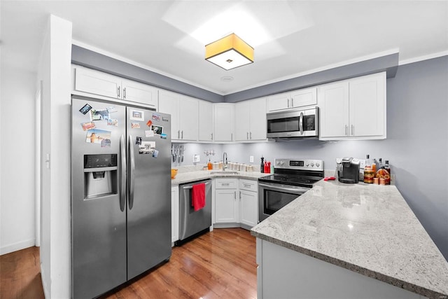 kitchen featuring appliances with stainless steel finishes, light stone counters, sink, white cabinets, and light hardwood / wood-style floors