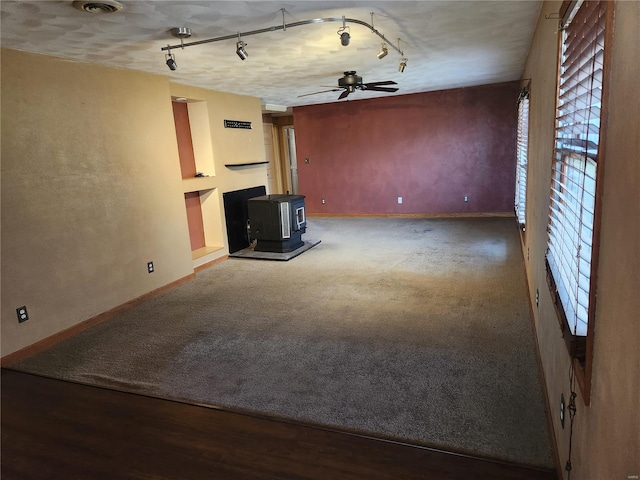 unfurnished living room featuring rail lighting, a textured ceiling, ceiling fan, hardwood / wood-style floors, and a wood stove