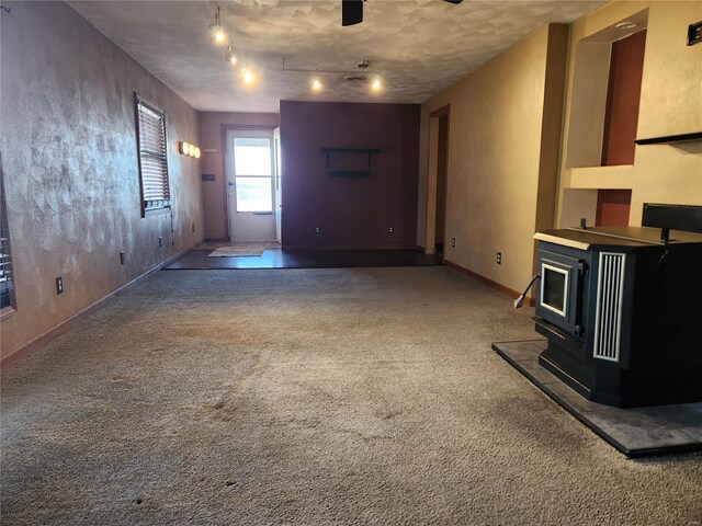 unfurnished living room featuring carpet flooring, a wood stove, a textured ceiling, and track lighting