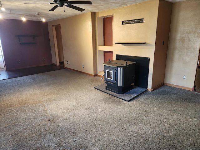 unfurnished living room featuring a wood stove, ceiling fan, and carpet floors