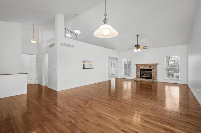 unfurnished living room featuring a fireplace, hardwood / wood-style floors, high vaulted ceiling, and ceiling fan