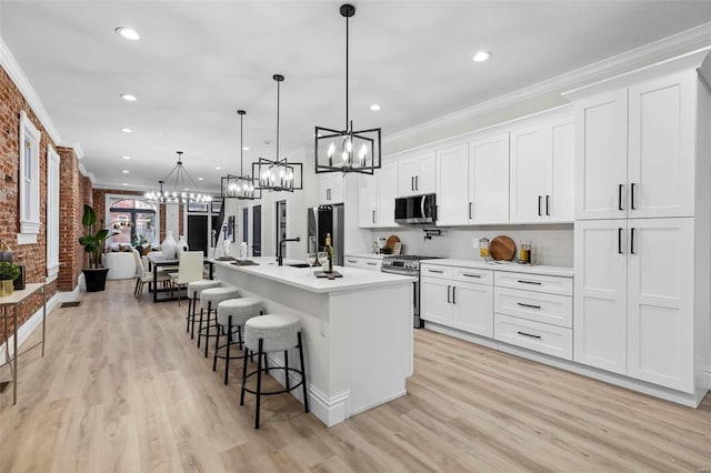 kitchen featuring white cabinets, decorative light fixtures, a center island with sink, and appliances with stainless steel finishes