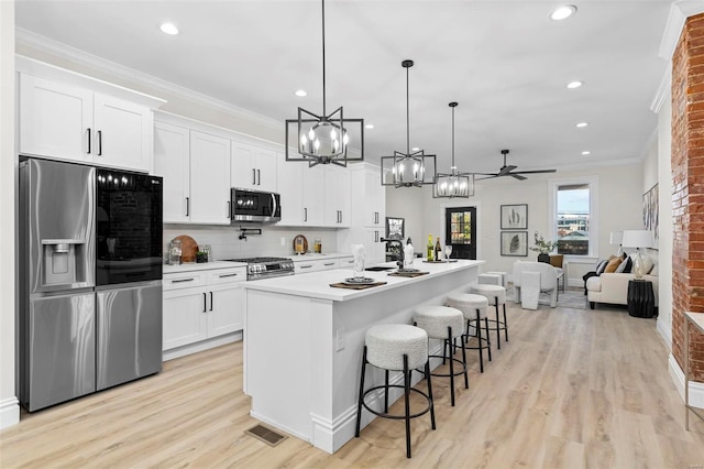 kitchen with ceiling fan, hanging light fixtures, stainless steel appliances, a kitchen island with sink, and white cabinets