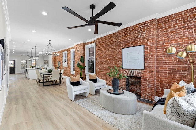 living room with ceiling fan with notable chandelier, ornamental molding, brick wall, and light hardwood / wood-style flooring