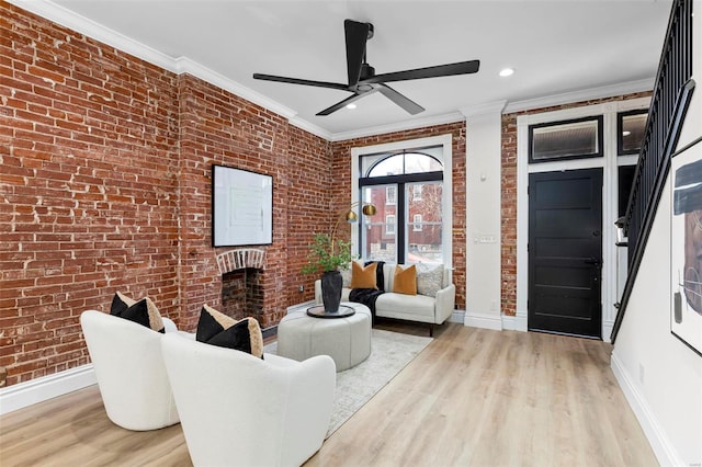 living room with ceiling fan, light hardwood / wood-style flooring, brick wall, and ornamental molding