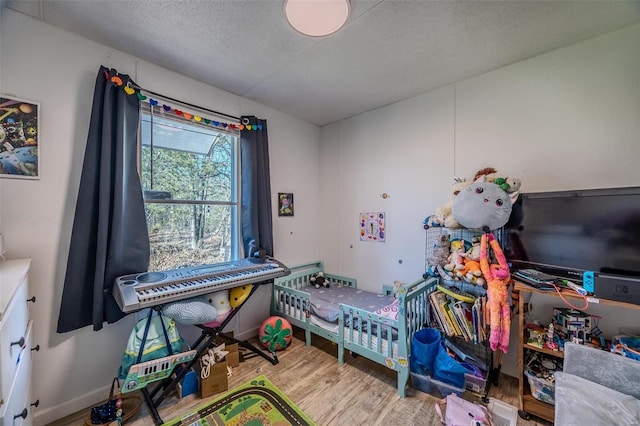 bedroom featuring a nursery area, wood-type flooring, and a textured ceiling