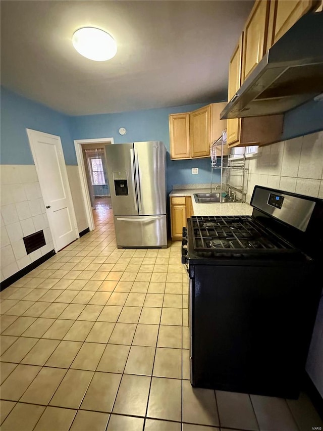 kitchen featuring sink, stainless steel fridge, black gas range oven, tasteful backsplash, and light tile patterned flooring