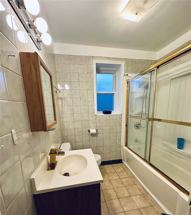 full bathroom with vanity, combined bath / shower with glass door, tile patterned flooring, toilet, and tile walls