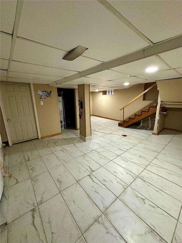 basement with a paneled ceiling and water heater