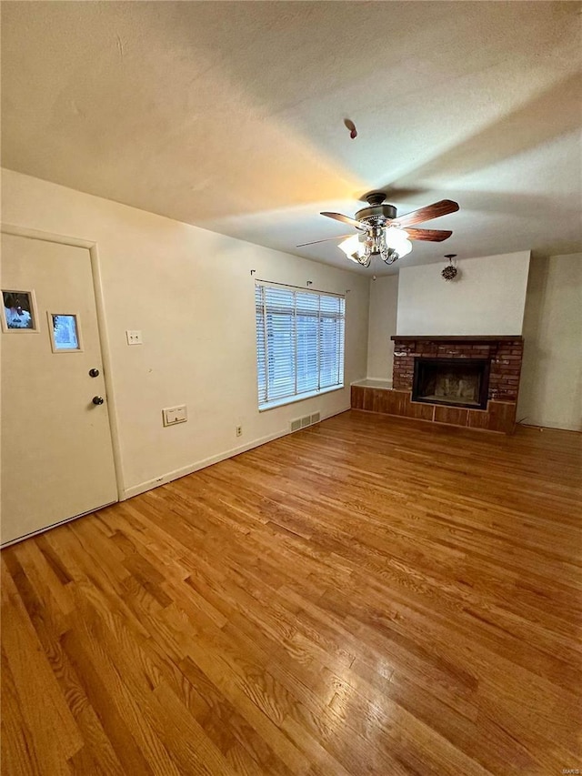 unfurnished living room with a stone fireplace, ceiling fan, a textured ceiling, and hardwood / wood-style flooring