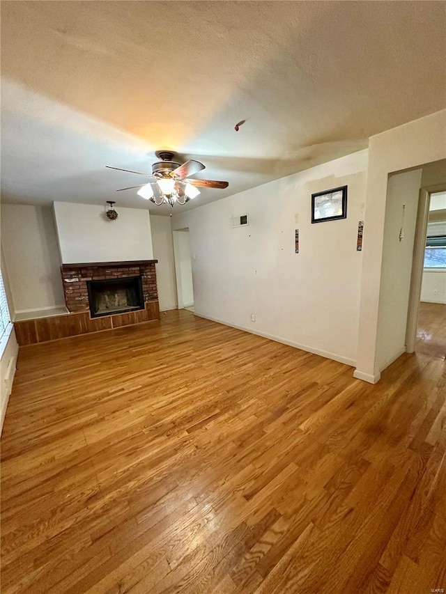 unfurnished living room with a textured ceiling, ceiling fan, light hardwood / wood-style floors, and a fireplace