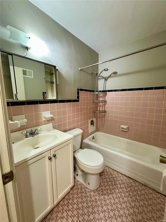 full bathroom featuring vanity, tiled shower / bath combo, tile walls, and toilet