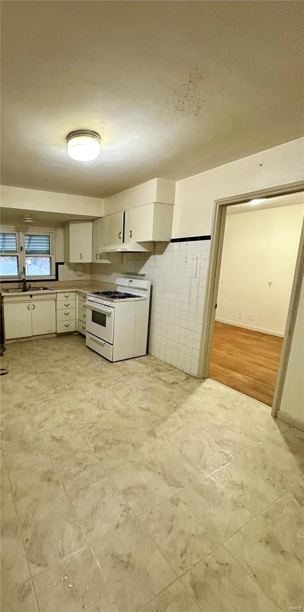 kitchen with white gas range oven, light hardwood / wood-style flooring, tile walls, and sink