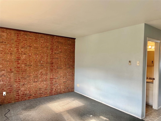 carpeted spare room with brick wall