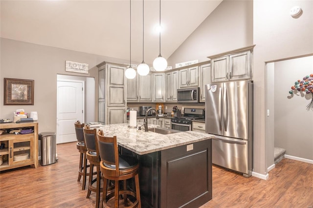 kitchen with sink, light stone counters, hardwood / wood-style floors, an island with sink, and appliances with stainless steel finishes