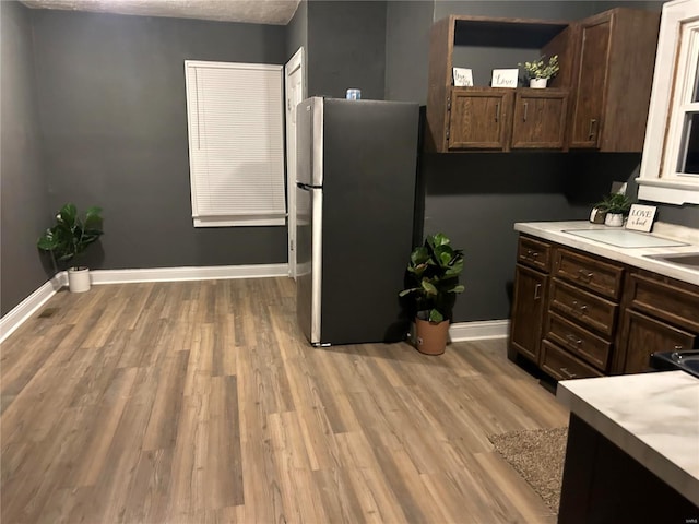 kitchen with dark brown cabinets, light hardwood / wood-style floors, stainless steel refrigerator, and sink