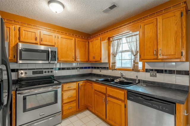 kitchen featuring sink, light tile patterned flooring, a textured ceiling, and appliances with stainless steel finishes