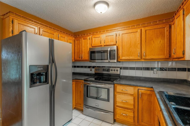 kitchen with sink, tasteful backsplash, a textured ceiling, light tile patterned floors, and appliances with stainless steel finishes