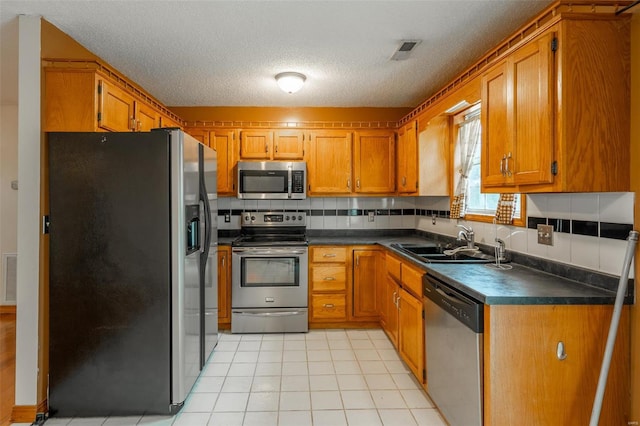 kitchen featuring backsplash, sink, a textured ceiling, light tile patterned flooring, and stainless steel appliances