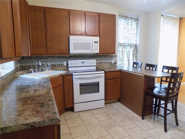 kitchen featuring a breakfast bar, white appliances, sink, light tile patterned floors, and kitchen peninsula