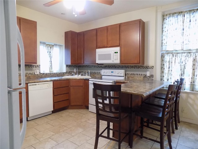 kitchen featuring white appliances, backsplash, sink, a kitchen bar, and kitchen peninsula