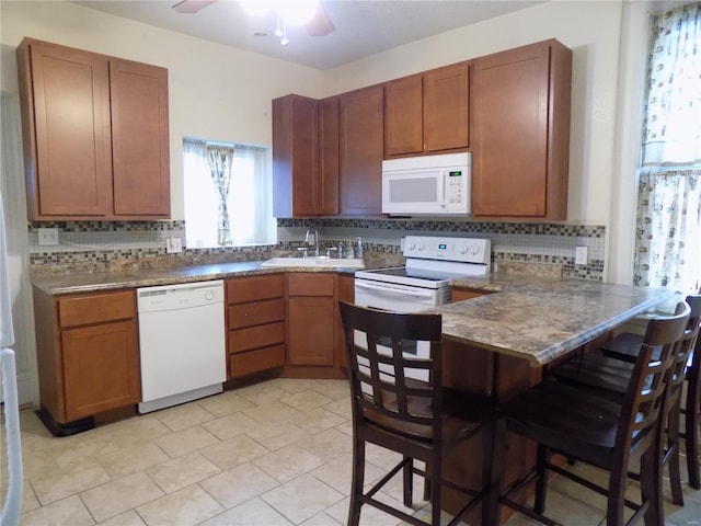 kitchen with kitchen peninsula, a kitchen breakfast bar, backsplash, white appliances, and sink