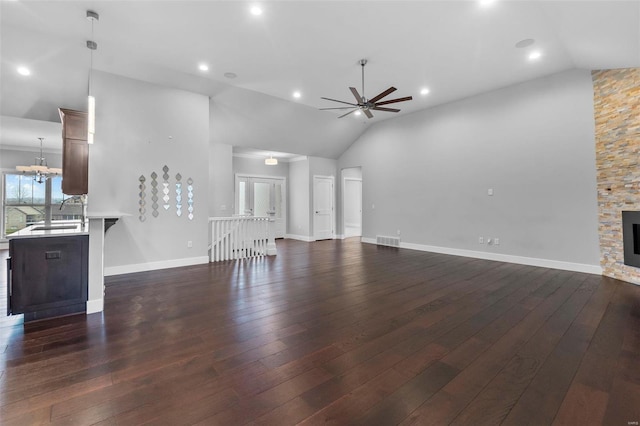 unfurnished living room featuring a fireplace, high vaulted ceiling, dark wood-type flooring, and ceiling fan with notable chandelier