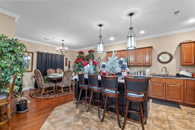 kitchen with a kitchen bar, ornamental molding, sink, light hardwood / wood-style floors, and hanging light fixtures