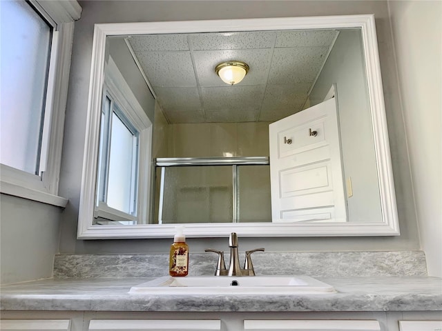 interior details with a shower with door, a paneled ceiling, and vanity